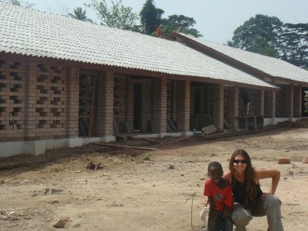 Fotografia de Ana Livi com uma criança próximos a uma construção de provável escola