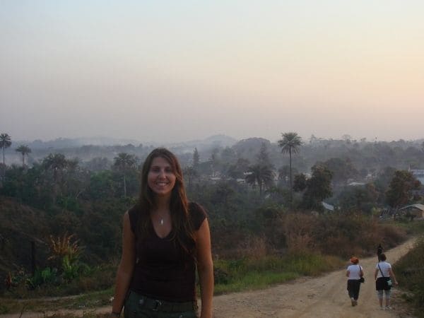 Fotografia de Ana Livi em uma estrada de cascalho com uma vila ao fundo