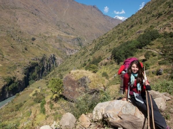 Fotografia de Ana Livi sentada em uma rocha descançando em uma montanha íngrime segurando bastões para auxiliar na caminhada e carregando uma mochila nas costas